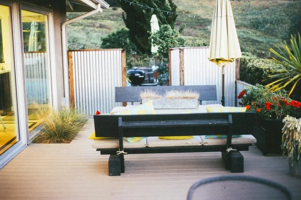 A sunny backyard deck with a wooden bench, a table and potted plants