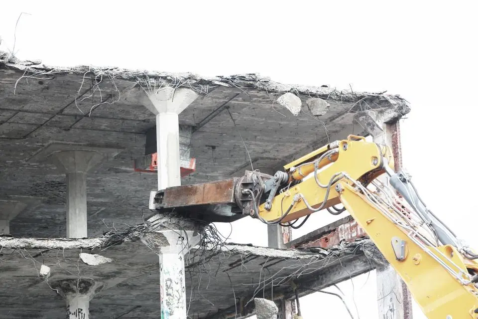 A yellow excavator arm tearing down a concrete floor slab during a demolition