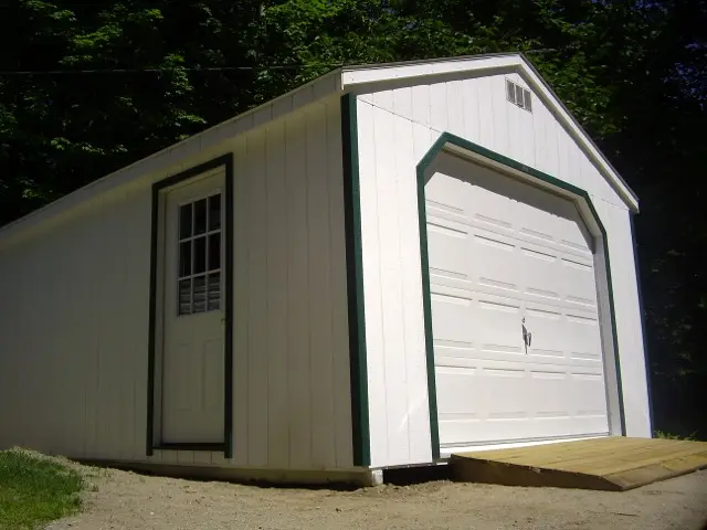 A small white detached garage with a single overhead door, a side door and a wooden entry ramp