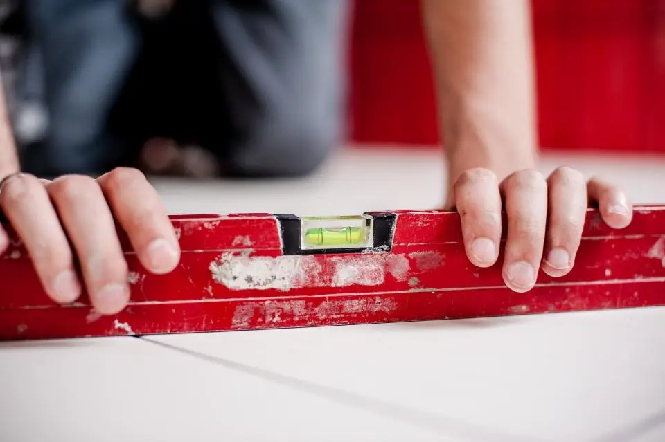 Two hands holding a red spirit level flat on a white surface