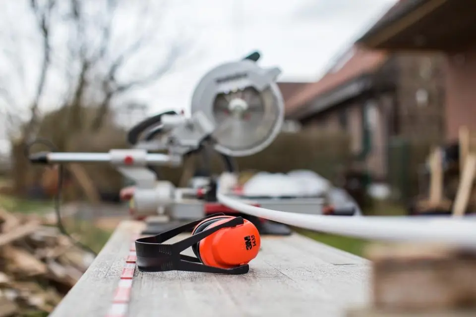 A miter saw and orange ear protection on a workbench outside a house under construction