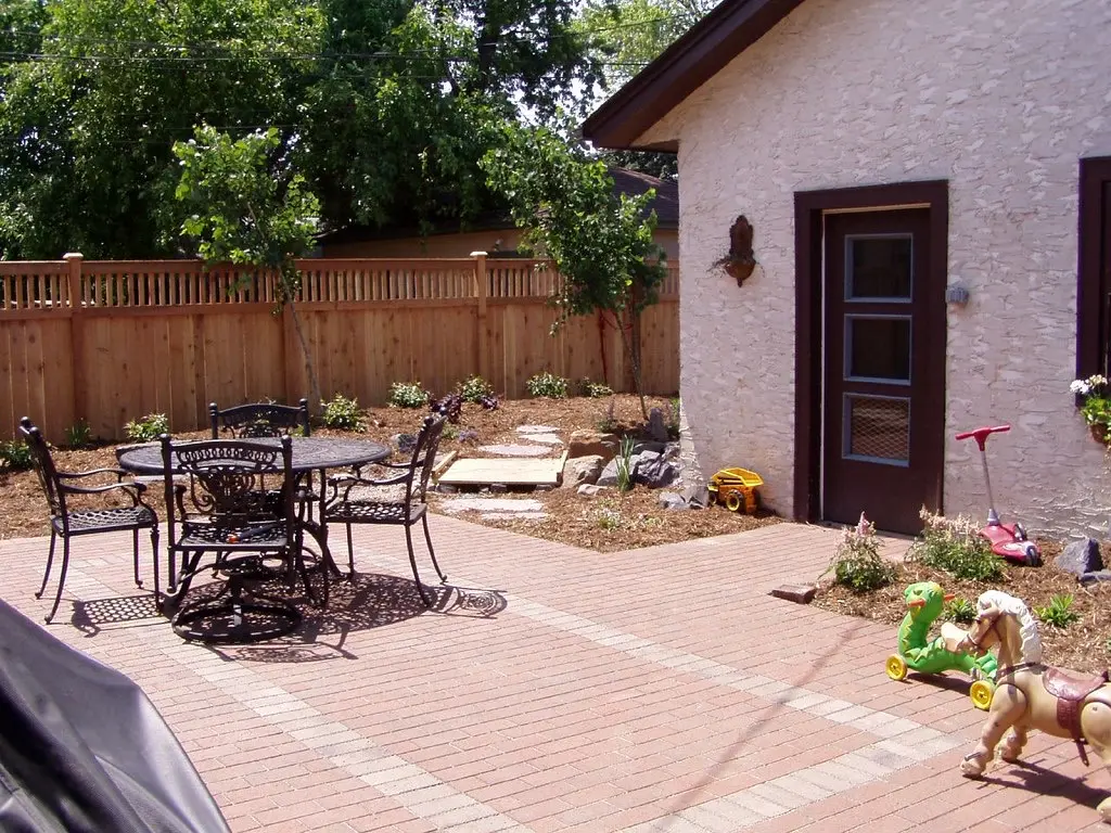 A brick paver patio with a metal table and chairs next to a white garden building