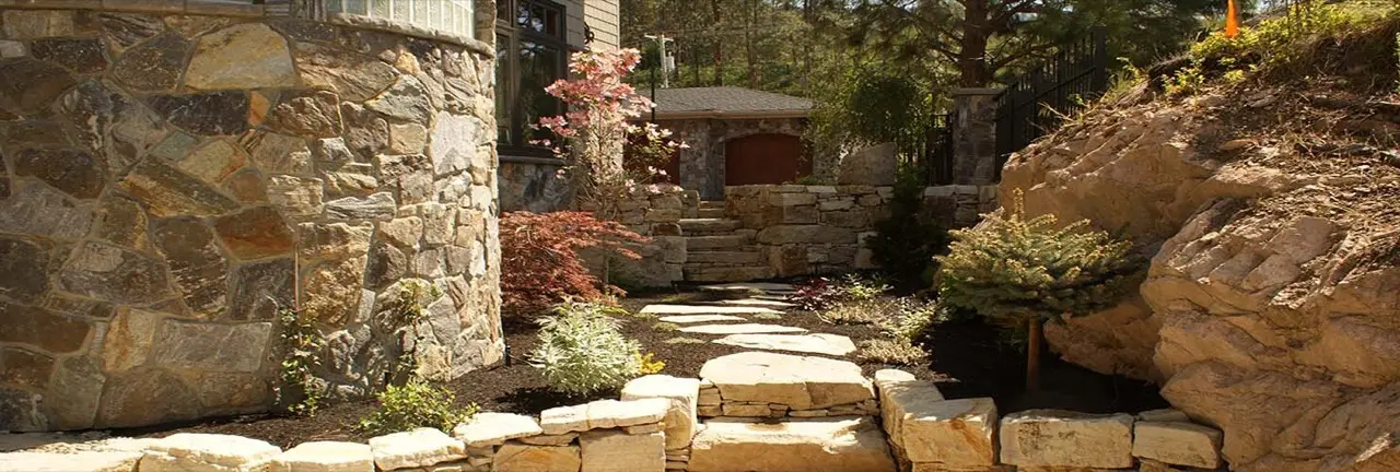 Low natural stone retaining walls forming terraced garden beds beside a stone path