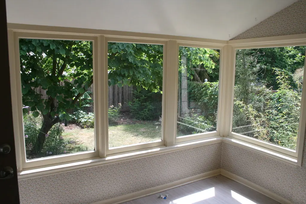 An empty sunroom with walls of large windows looking out on a leafy garden