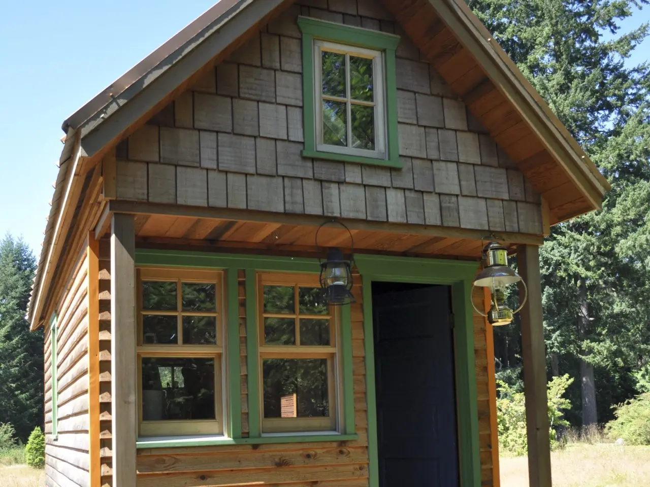 A small cedar-shingled tiny house with green window trim and a covered front porch in Portland, Oregon