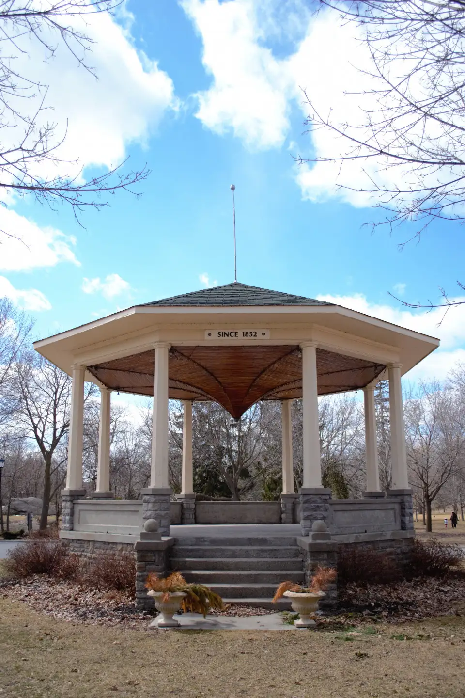 A white octagonal gazebo with a shingled roof and front steps under a blue sky